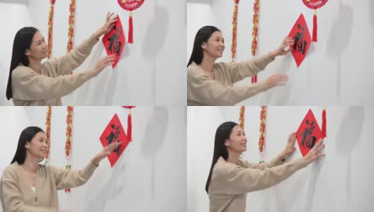 快乐的亚洲妇女在准备中国新年期间贴在墙上的汉字“财富”春联高清在线视频素材下载