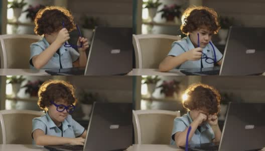 一个戴眼镜的男孩坐在笔记本电脑前，因疲劳而揉眼睛高清在线视频素材下载