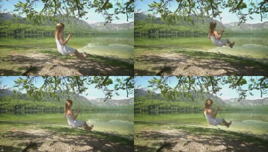 身穿白裙的女孩在湖边的绳上荡秋千高清在线视频素材下载