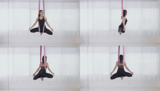 活跃的运动年轻的亚洲妇女在丝绸瑜伽吊床上做空中练习莲花姿势。柔韧性和专注力，反重力放松健身理念。漂亮年轻的亚洲妇女在黑色运动服做瑜伽莲花姿势。高清在线视频素材下载