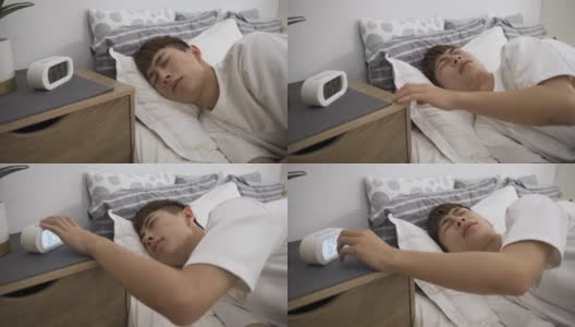 近景拍摄在床上睡觉的亚洲男孩正在关掉闹钟，在家里用一个鬼脸揉他的头，因为他有偏头痛。高清在线视频素材下载