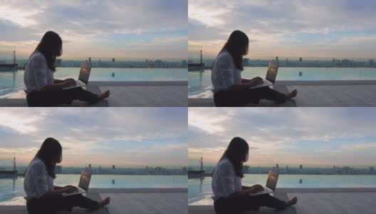 年轻女子在工作，用笔记本电脑坐在摩天大楼的泳池旁。自由职业，假期，远程工作，社会距离，电子学习，在线会议的概念。本空间高清在线视频素材下载