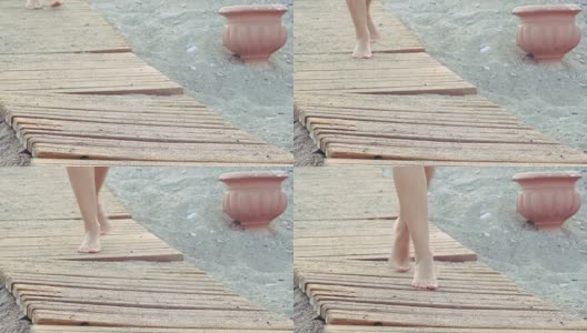 美丽的女性晒黑的脚走在海滩上的木制人行道上。女孩在沙滩上漫步高清在线视频素材下载