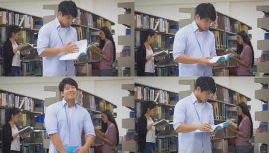 年轻快乐的亚洲学生男人在大学图书馆看书和她的同学在背景，教育和学校的理念高清在线视频素材下载
