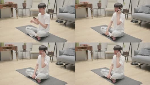 年轻的亚洲男子坐在瑜伽垫上用智能手机聊天高清在线视频素材下载