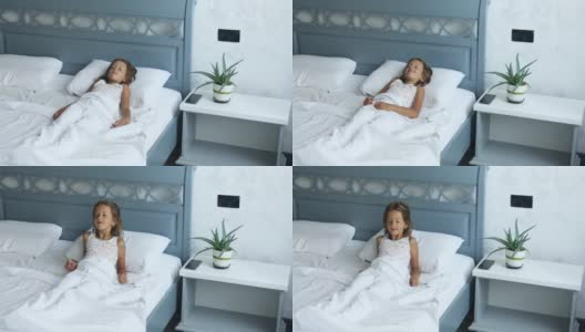 小女孩从家里一张又大又舒适的床上醒来，床上有白色的亚麻布高清在线视频素材下载