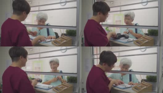 亚洲华人老年妇女用信用卡支付医药费，女护士手持信用卡读卡器在诊所刷卡高清在线视频素材下载