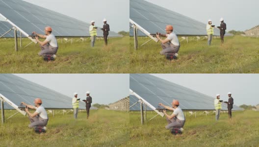 印度技术人员用万用表检查太阳能电池板。身穿制服的印度男子蹲在太阳能电池板附近，手里拿着万用表。两个商务人士用电子设备在背景上说话高清在线视频素材下载