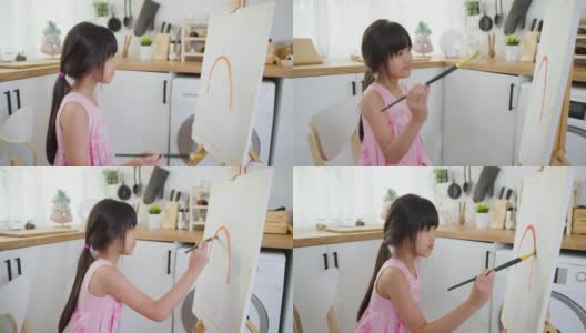 亚洲年轻快乐的小女孩在客厅的画板上画画。可爱的小朋友在家里学习如何用水彩画和毛笔画画，享受假期的创意活动。高清在线视频素材下载