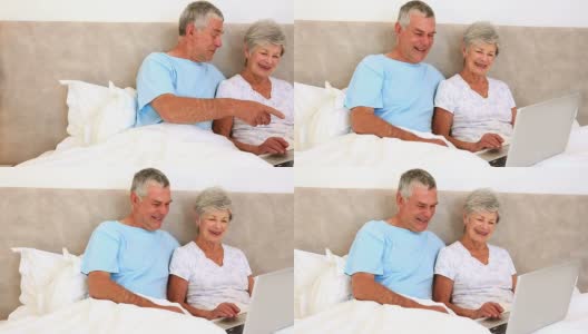 一对快乐的老年夫妇坐在床上用笔记本电脑高清在线视频素材下载