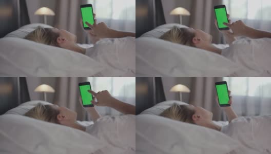 一个女人拿着一部绿色手机在床上闲逛。高清在线视频素材下载