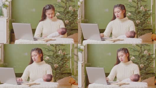 快乐的亚洲母亲妇女抱着她的婴儿新生儿和工作呆在家里。自由职业妈妈用电脑工作，在圣诞节前夕在家照顾她的新生儿高清在线视频素材下载