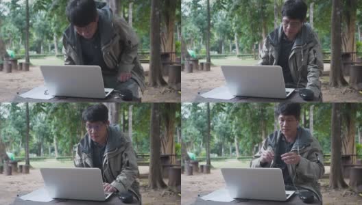 亚洲男人用森林背景的笔记本电脑工作。男性除了在家和办公室外，还会在旅行时在线工作。高清在线视频素材下载