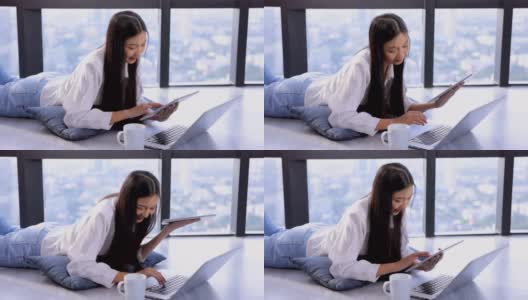 一名年轻的亚洲女性，双腿翘起，躺在地板上，在家用笔记本电脑或平板电脑观看在线数字课程，帮助员工提高技能。商学院为成人提供课程教育高清在线视频素材下载