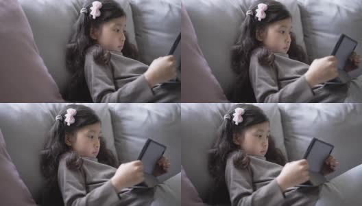 小女孩在家里的客厅里用数码平板电脑在线学习高清在线视频素材下载