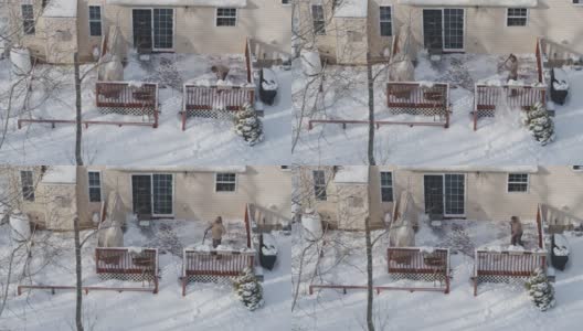 一个成年人在冬天下雪后用铲子清理门廊上的积雪。鸟瞰图直接在无人机视频上方。高清在线视频素材下载