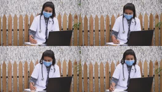 女医生坐在医院的桌子上用笔记本电脑开处方。医生在诊所戴口罩高清在线视频素材下载