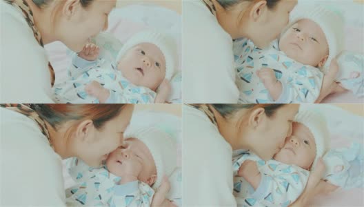 快乐的亚洲母亲抱着和亲吻她的混血可爱的小新生儿的脸颊在她的卧室高清在线视频素材下载