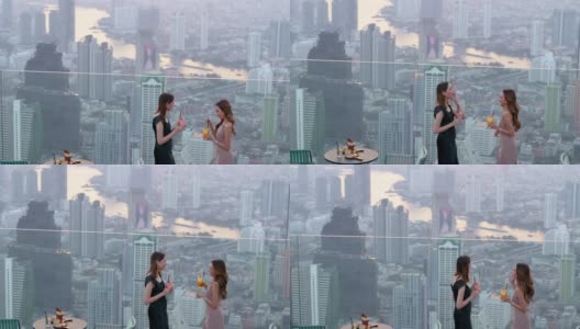 4K亚洲女性朋友在夏日夕阳下，在摩天大楼的屋顶餐厅一起喝鸡尾酒聊天。高清在线视频素材下载