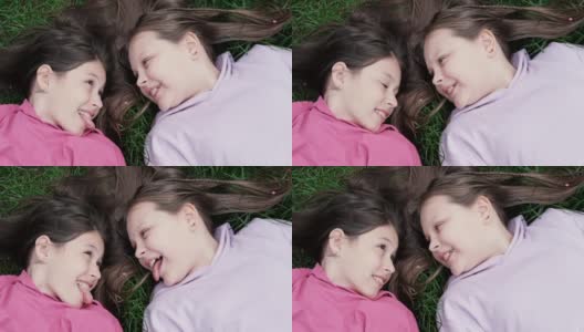 两个漂亮的千禧一代朋友躺在公园或草坪上的绿草地上。白人女孩笑着一起玩。俯视图的镜头高清在线视频素材下载