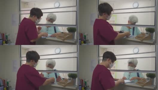 亚裔华裔老年妇女戴着口罩，在诊所用信用卡刷卡，女护士拿着信用卡读卡器高清在线视频素材下载