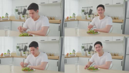 亚洲活跃的帅哥拒绝吃甜甜圈，喜欢吃健康食品。年轻有魅力的男性，在厨房的碗里吃蔬菜沙拉，在桌子上喝干净的水。饮食与健康理念高清在线视频素材下载