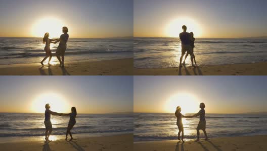 在美丽的海滩上，年轻的夫妇手牵着手，在夕阳下旋转。高清在线视频素材下载