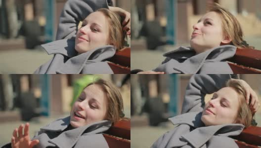 年轻女子坐在户外长椅上，面带微笑，目光移开。高清在线视频素材下载