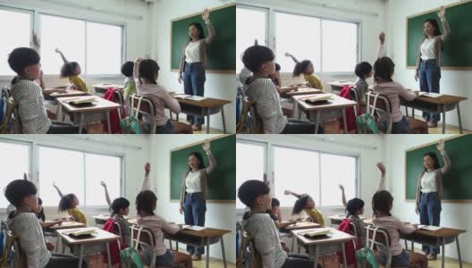 一群小学生拿着笔记本坐在教室里，举手回答老师的问题。教育，小学，学习，回到学校的概念高清在线视频素材下载