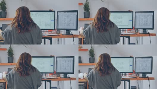在一个高层建筑的项目中，一个女人用笔记本电脑和两个额外的显示器工作的背影。使用远程方案在家工作的概念。检疫高清在线视频素材下载