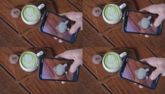 美食博主用手机拍摄热抹茶拿铁，在社交媒体、在线、数字生活方式中获取新内容。垂直拍摄。在木桌上放着一大杯热饮，上面有红心形状的泡沫高清在线视频素材下载