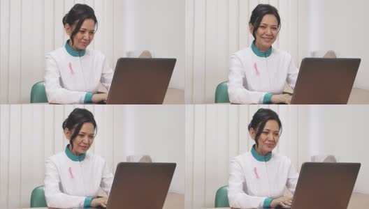 一名女治疗师，实验服上别着粉色丝带，在笔记本电脑上工作高清在线视频素材下载