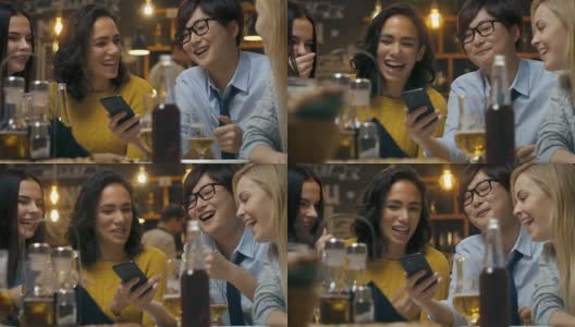 当朋友们在酒吧玩得开心时，年轻的亚洲男子在他的智能手机上向他们展示有趣的东西。他们在时尚的时髦酒吧里大笑，开玩笑，喝酒。高清在线视频素材下载
