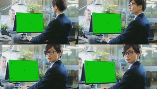 在办公室里，东亚商人在一台模拟绿色屏幕的台式个人电脑上工作。他戏剧性地转头，越过肩膀看向镜头。同事走进办公室，并在她的办公桌前发生。高清在线视频素材下载
