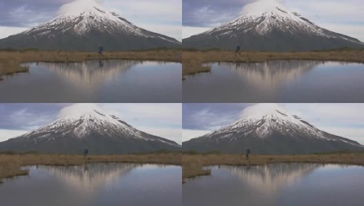 慢动作-旅行者步行横向观看塔拉纳基火山在北岛的新西兰和反射山和登山者在湖中。新西兰被高清在线视频素材下载