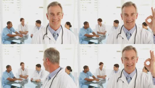 快乐的医生看着摄像机和他身后的工作人员高清在线视频素材下载