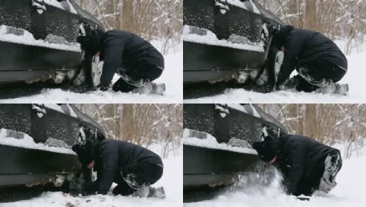 一名男子在汽车车轮附近清理积雪。高清在线视频素材下载