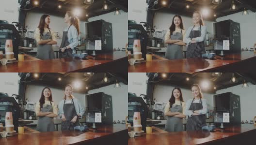两名年轻美丽的亚洲女咖啡师穿着围裙，微笑着站在咖啡馆的吧台边交谈。咖啡店和小型咖啡店的概念。缓慢的运动。高清在线视频素材下载