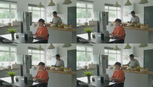 亚洲中国妇女在家工作，丈夫在厨房柜台准备午餐高清在线视频素材下载