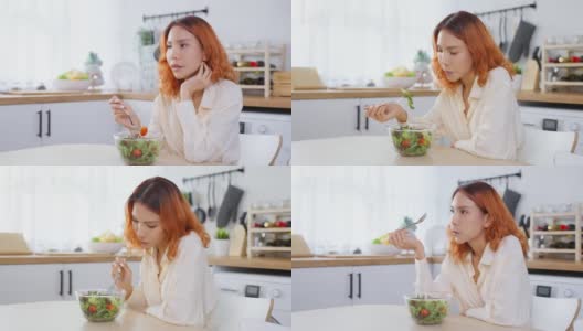 亚洲有吸引力的女人在家里厨房的桌子上吃绿色沙拉。年轻美丽的素食女孩感到快乐，享受早餐蔬菜健康的食物，在家里减肥健康。高清在线视频素材下载
