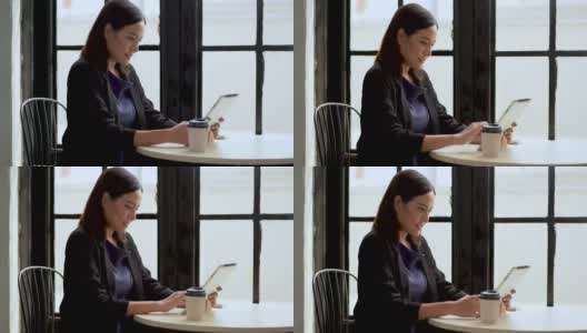 亚洲女商人用数码平板电脑喝咖啡在咖啡店或餐厅的窗户上休息一下高清在线视频素材下载