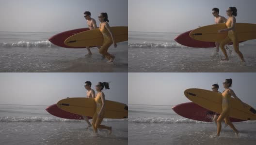 带着冲浪板冲进海浪的快乐夫妇。高清在线视频素材下载
