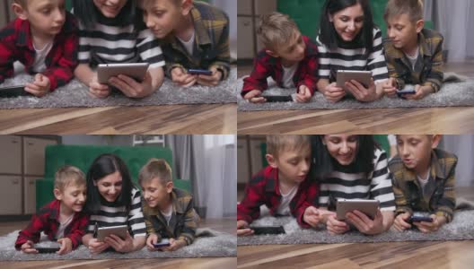 正面的看法，善良的微笑，爱的母亲和两个儿子休息在家里的地板上，在i-pad上观看有趣的视频高清在线视频素材下载