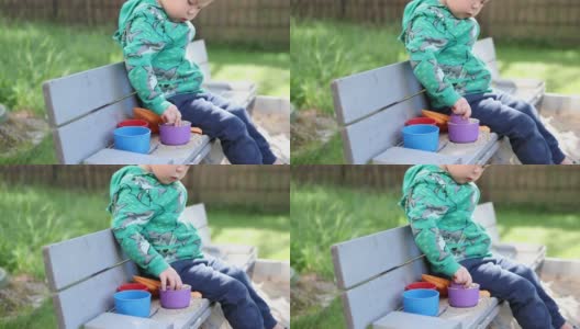 白种人小孩男孩在阳光明媚的日子里在院子外面玩沙盒沙塑料模具高清在线视频素材下载