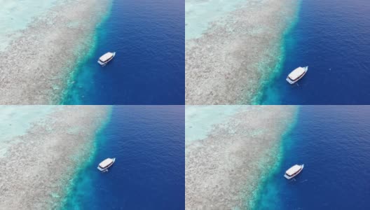 无人机在热带岛屿上空飞向漂浮在深蓝色海水上的水肺潜水船，Alif Alif环礁，Rasdhoo，马尔代夫，印度洋。白沙碧水。高清在线视频素材下载