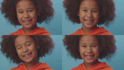 近距离的微笑非洲裔美国女孩穿着橙色的衣服看着镜头在蓝色的背景。7岁的快乐孩子。高清在线视频素材下载