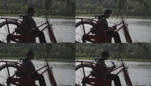 坐在自行车旁边的人在湖边扔纸飞机。高清在线视频素材下载