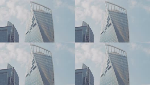 蓝色多云的天空背景下扭曲的摩天大楼的底部视图。行动。玻璃幕墙高层建筑在商业城市中心。高清在线视频素材下载