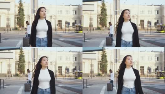 和蔼微笑的年轻时尚的亚洲妇女走在城市街道上的铁路或汽车站的背景高清在线视频素材下载