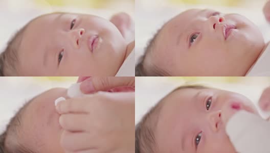 母亲用棉垫清洁新生儿的眼睛。新生儿看着妈妈用爱擦干她的身体。新生儿护理概念高清在线视频素材下载
